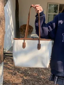 Detail view of a vintage large capacity tote bag in off-white and brown held outdoors