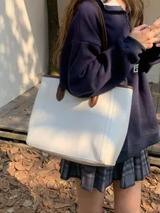 Minimalist vintage white tote bag with brown leather straps worn by a woman outdoors
