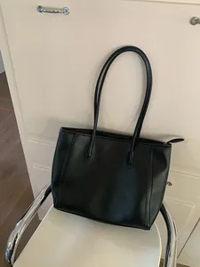 Detail view of a black vintage-style large capacity tote bag placed on a white chair