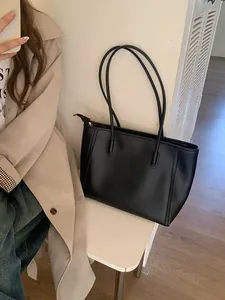 Modern black faux leather tote bag with long handles in a stylish lifestyle setting