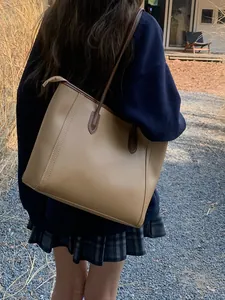 Back view of a woman carrying a minimalist khaki retro leather tote bag in a garden