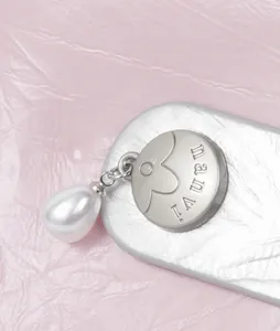 Macro detail view of silver wallet hardware featuring an engraved logo and a pearl charm