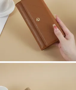 Close-up of a brown quilted long wallet held by a hand in a minimalist beige setting