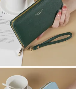 Dettaglio di un portafoglio lungo in pelle saffiano verde scuro con cinturino e zip d'oro.