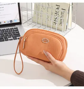 Detailed view of an orange double-zipper clutch bag held by hand in a workspace