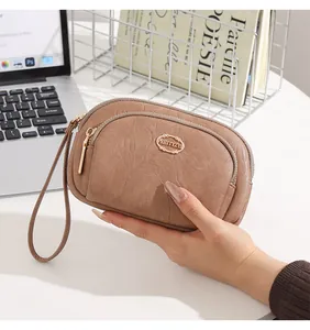 Close-up of a hand holding a brown double zipper PU leather clutch for phone and keys