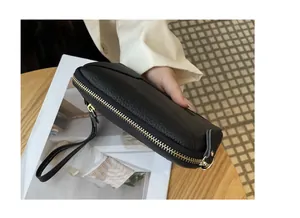 Detailed close-up of a black litchi grain leather wristlet with a golden metal zipper