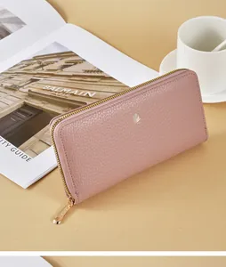 Detail shot of a pink pebbled leather long wallet with golden zipper on a tan background