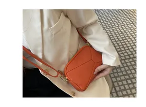 Detail view of a vibrant orange pebble grain leather crossbody phone bag worn with white blazer