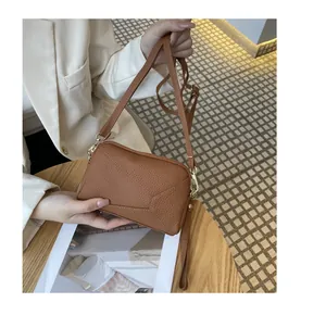 Close-up of a brown leather crossbody phone bag with geometric stitching held by hand