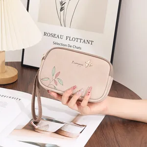 Detailed view of beige double zipper clutch with colorful leaf print and gold bird emblem