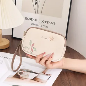 Macro view of cream-colored floral clutch bag with golden bird charm and wrist strap