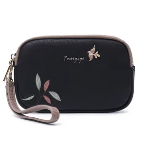 Close-up view of black women's clutch bag with leaf print and gold metal bird charm.