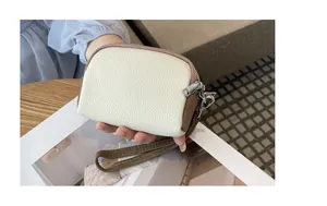 Dettaglio di un borsellino in pelle con cinturino da polso e tripla zip laterale.