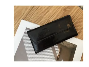 Primer plano de cartera larga de cuero negro con textura agrietada sobre madera.