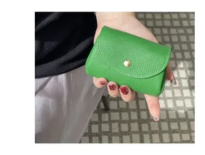 Close-up showing the pebble grain texture of a mini green leather coin purse in hand.
