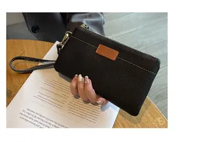 Detail view of a black pebbled leather clutch with a wrist strap and white stitching.