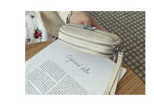 Detailed view showing the textured beige pebbled leather and double zippers of this mini coin purse.