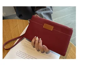 Close-up of a red pebbled leather wristlet clutch with gold zipper and white stitching