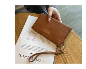 Close-up of a brown leather wristlet pouch on a wooden table with detail on stitching.