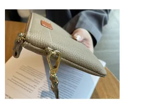 Close-up of beige pebbled leather coin purse with golden zipper and clip details.