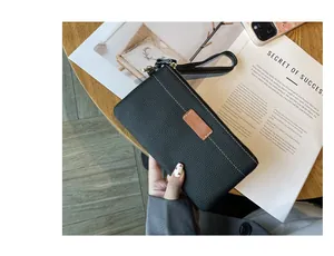 Close-up detail of black pebbled leather wristlet clutch with elegant brown accent patch
