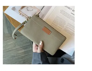 Close-up of a khaki litchi grain leather clutch bag with a brown patch detail
