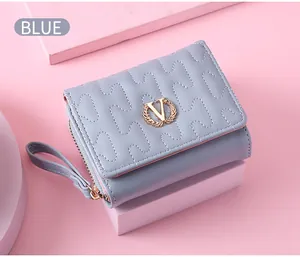 Close-up of light blue quilted wallet with gold wreath V logo on pink background.