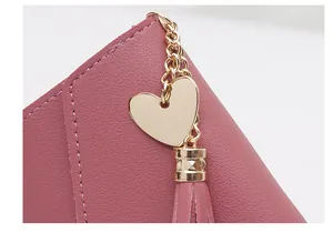 Close-up detail of a dusty pink leather wallet featuring a gold heart charm and tassel