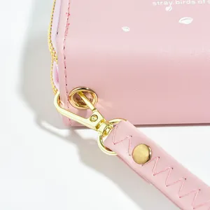 Primo piano di un portafoglio rosa con doppia cerniera, motivo a cuore e cinturino da polso
