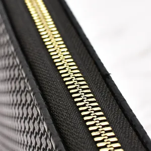 Detail view of a premium black woven long wallet featuring a smooth gold zipper track