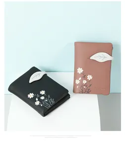 Close-up of two compact wallets with elegant daisy print and leaf-shaped strap closure