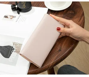 Detail of elegant pink long tri-fold clutch wallet held by hand on wooden table