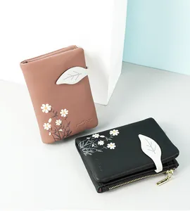 Close-up of small bi-fold wallets with daisy prints and leaf-shaped magnetic buckle