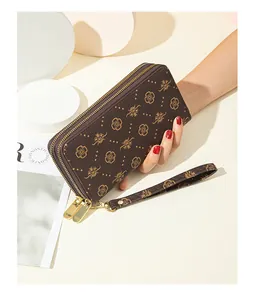 Detailed view of a brown patterned double-zipper long wallet held by a model's hand