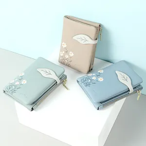 Compact women's bifold wallet with daisy floral print and leaf-shaped buckle detail.