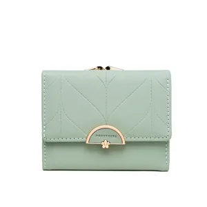 Detalle de cartera triple verde salvia con cierre metálico semicircular y adorno floral.