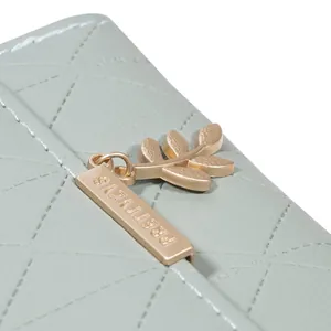 Detail shot of the gold leaf pendant and quilted pattern on a green women's tri-fold wallet
