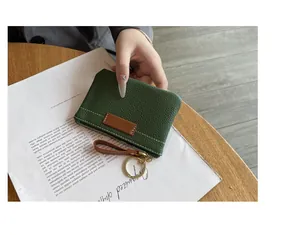 Détail d'un porte-monnaie compact en cuir grainé vert avec anneau porte-clés à la main