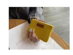 Détail d'un porte-monnaie en cuir jaune texturé tenu à la main sur un magazine