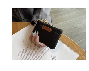 Gros plan d'un petit porte-monnaie en similicuir noir tenu à la main sur un magazine.
