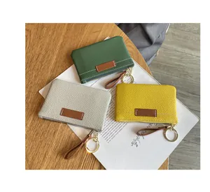 Gros plan de trois mini porte-monnaie colorés en cuir posés sur un magazine et du bois.