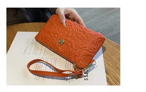 Détail d'une pochette en cuir orange gaufré avec un fermoir en forme de fleur dorée