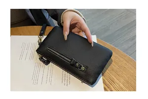 Gros plan sur la texture cuir noir grainé d'un portefeuille à dragonne chic