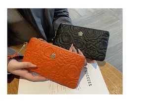 Détail des pochettes en cuir à gaufrage floral en orange vif et noir tenues à la main