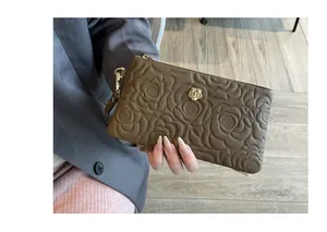 Vue détaillée de la pochette en cuir marron avec motif camélia gaufré et logo fleur dorée