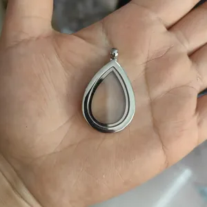Detailed macro shot of a silver teardrop-shaped floating locket pendant held in a hand