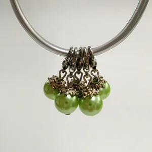 Close-up of light green pearl charms with silver lobster clasps and flower caps.