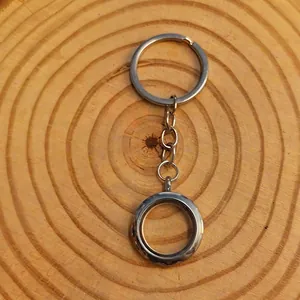 Detailopname van een ronde zilveren zwevende medaillon sleutelhanger op hout.