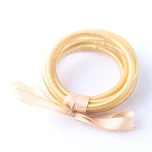 Dettaglio di braccialetti flessibili in silicone con foglia d'oro e un nastro di raso.